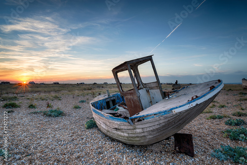 Wooden fishing boat with nets washed up on a shingle beach