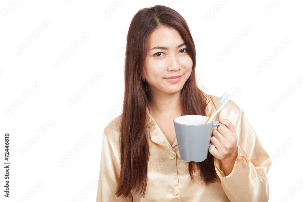 Asian woman in pajamas with toothbrush in mug Asian woman in pajamas with toothbrush in mug
