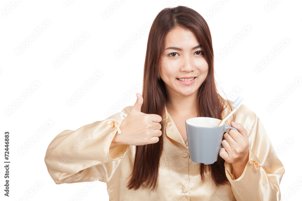 Asian woman in pajamas thumbs up with toothbrush in mug Asian woman in pajamas thumbs up with toothbrush in mug