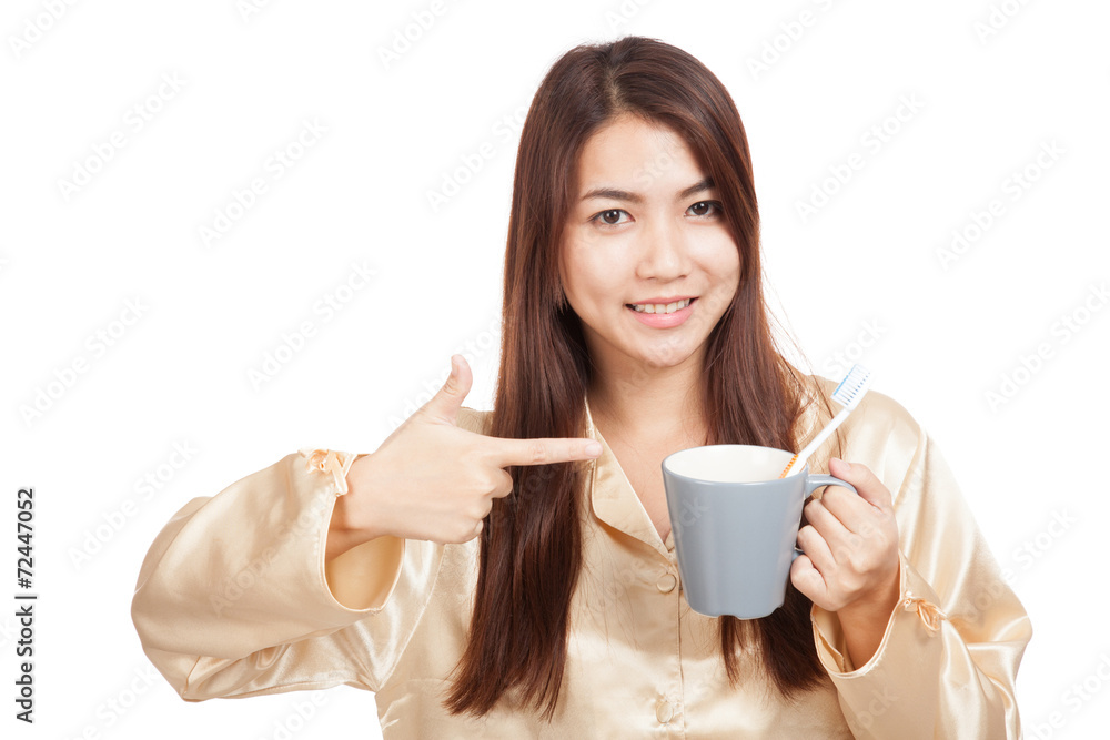 Asian woman in pajamas point to toothbrush in mug Asian woman in pajamas point to toothbrush in mug