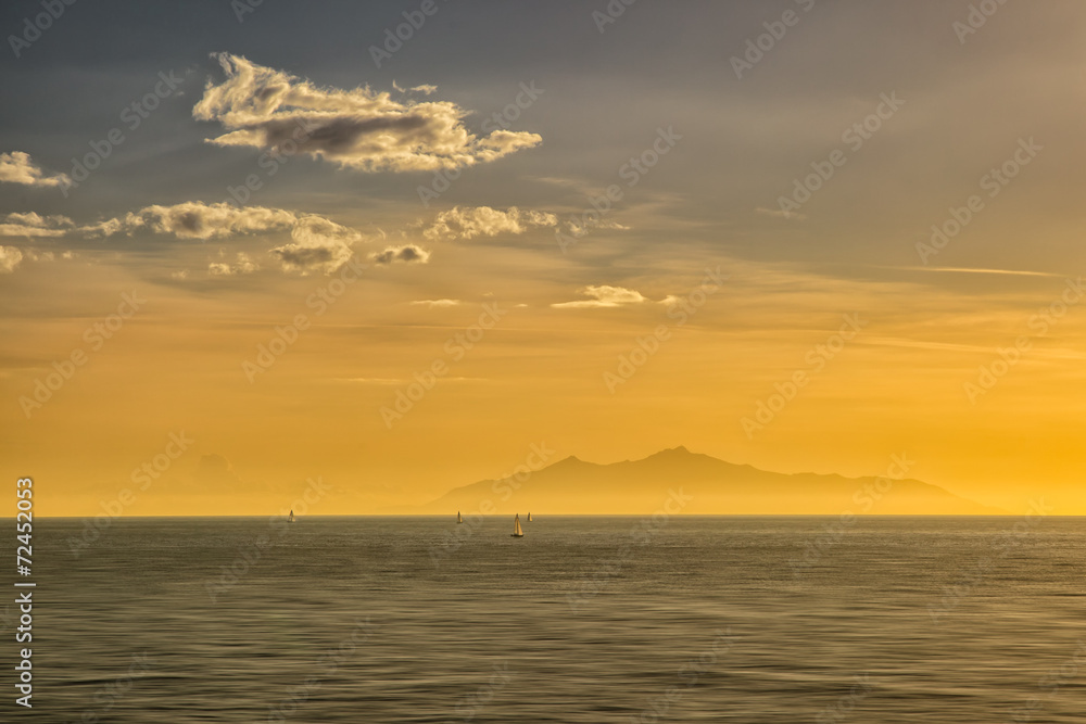 Sailing boats at sunrise against a silhouetted isle of Elba Sailing boats at sunrise against a silhouetted isle of Elba