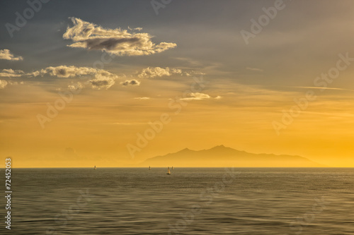 Sailing boats at sunrise against a silhouetted isle of Elba