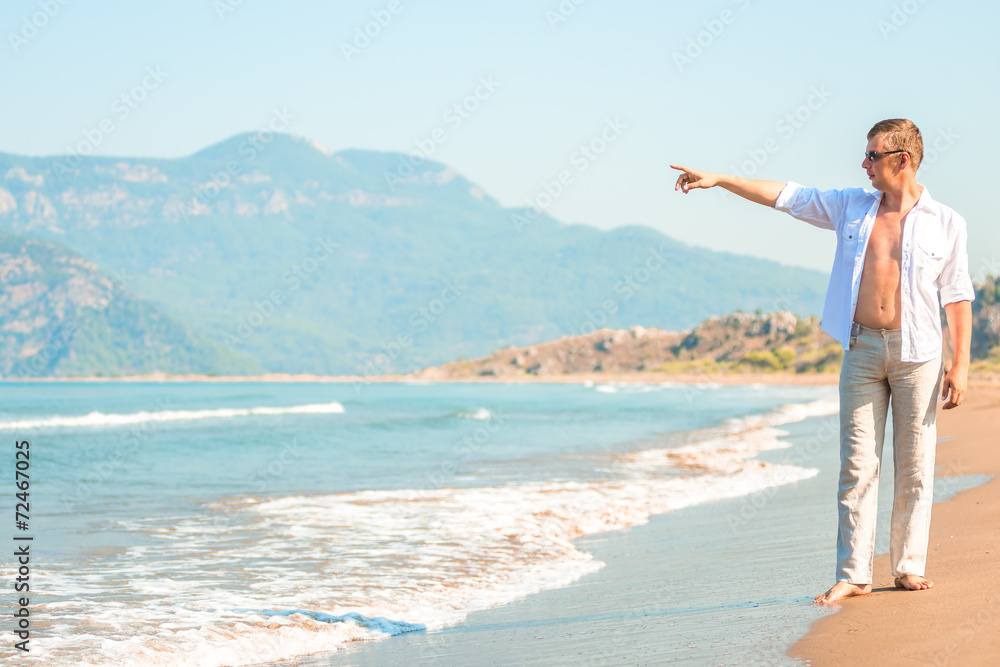 young man on the beach shows seaward