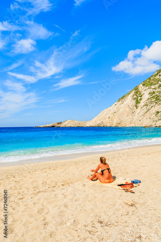 Young woman sitting on beautiful Petani beach, Kefalonia island