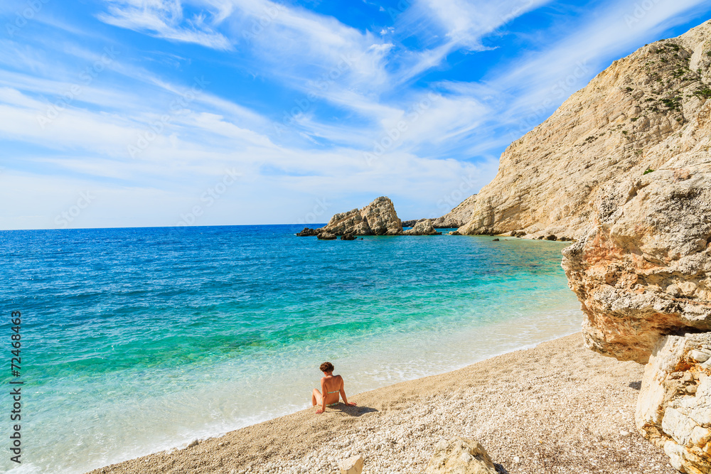 Young woman sitting on Petani beach, Kefalonia island, Greece