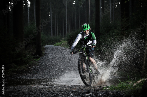 Mountain biker speeding through forest stream.