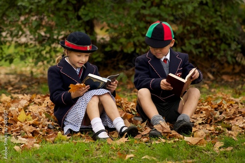 Brother and sister reading among autumn leaves