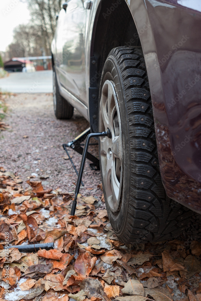 Studded tire wheel mounting on car with jack-screw at autumn Studded tire wheel mounting on car with jack-screw at autumn