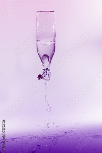 Clear water spill from a glass bottle on purple background on sh