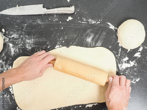 Person handling a dough with a rolling pin floured black table