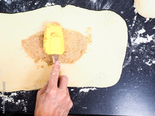 Person spreading cinnamon mix with spatula onto a flattened doug