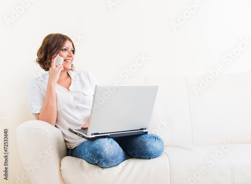 Woman using laptop and a phone on the sofa