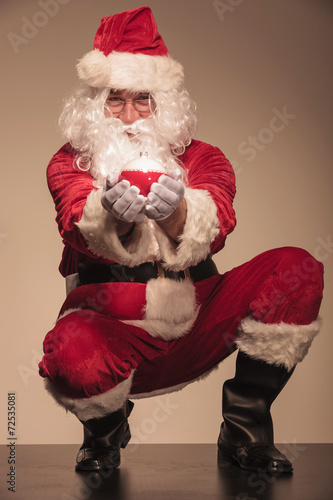 Santa sitting and presenting christmas ball. photo