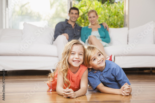 Happy children lying on floor, parents sitting on couch 