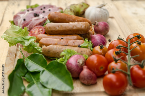 Fresh meat sausages and vegetables on kitchen board