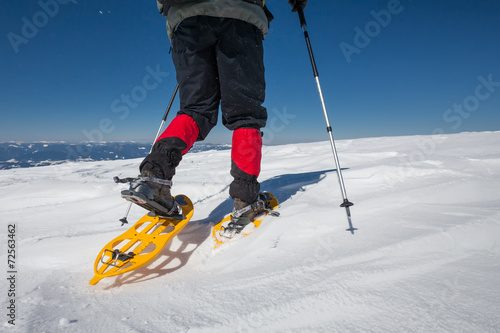 Hiker snowshoeing in winter mountains during sunny day