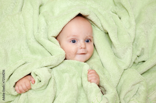 Caucasian baby boy covered with green towel joyfully smiles at c