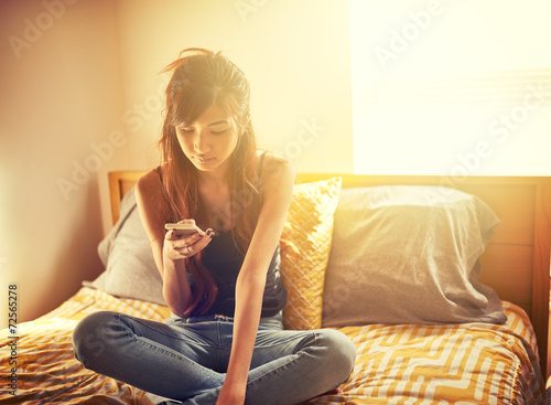 tech savvy asian teen girl using smart phone in bed