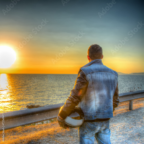 Biker with helmet looking at the sun at sunset