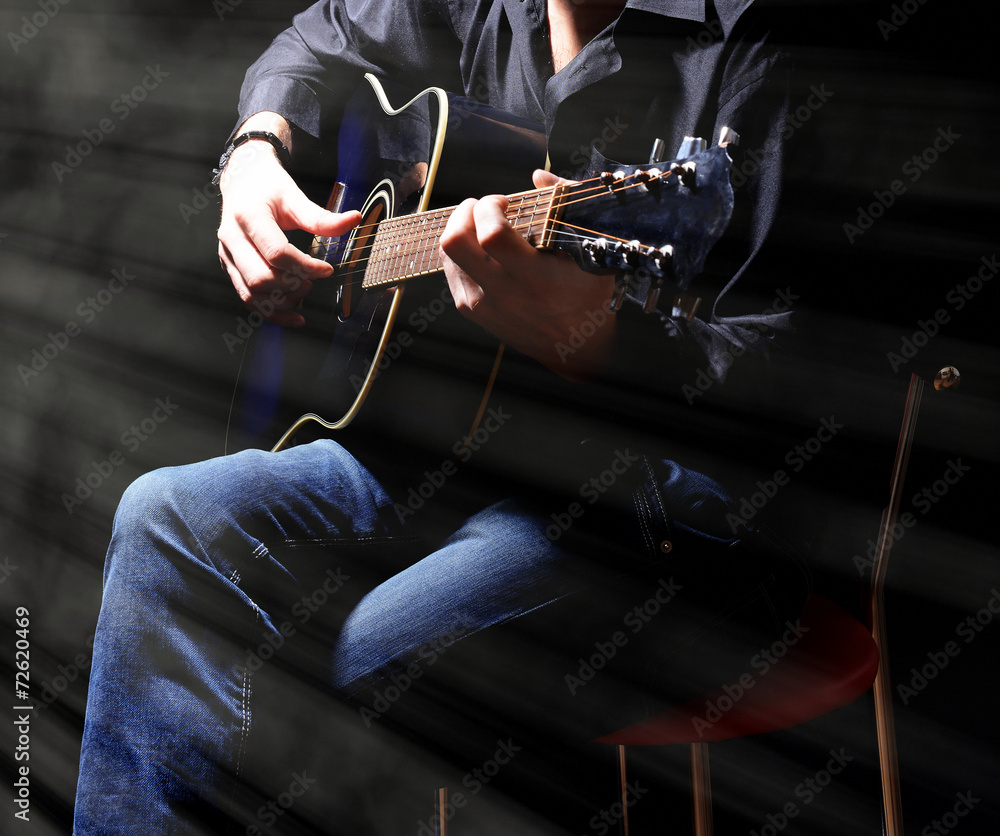 Obraz premium Young musician playing acoustic guitar on dark background