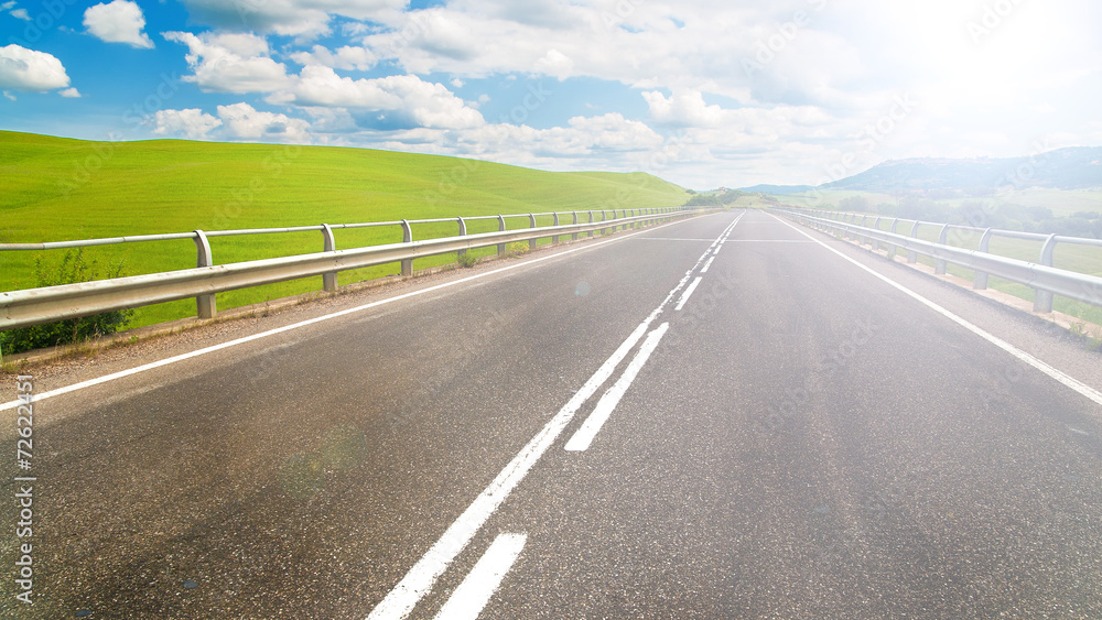 Long way between green fields with blue sky in the background