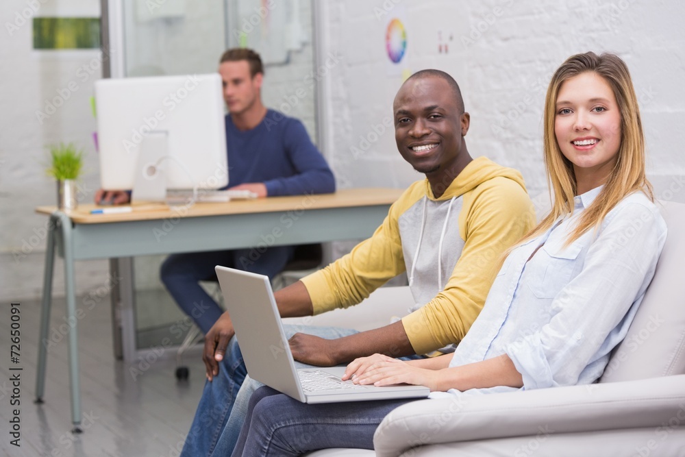 Casual colleagues using laptop on couch in office Casual colleagues using laptop on couch in office