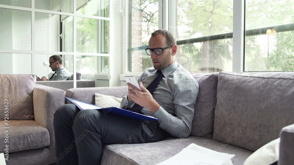 Businessman comparing data on smartphone and documents sitting o Businessman comparing data on smartphone and documents sitting o