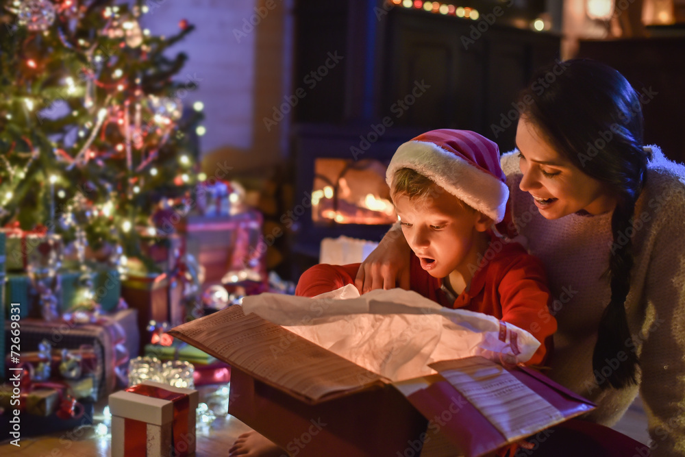 Lovely little boy with a santa claus hat and his mom opening a g
