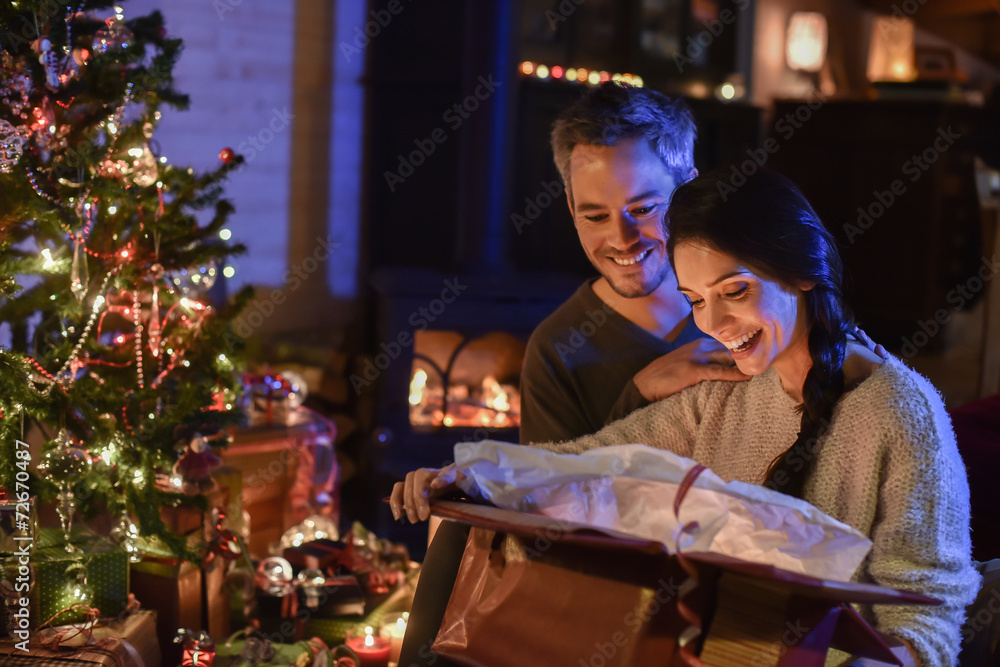 Handsome couple opening a gift in front of the Christmas tree li