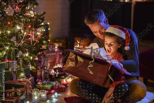 Lovely little girl with a santa claus hat and her father opening