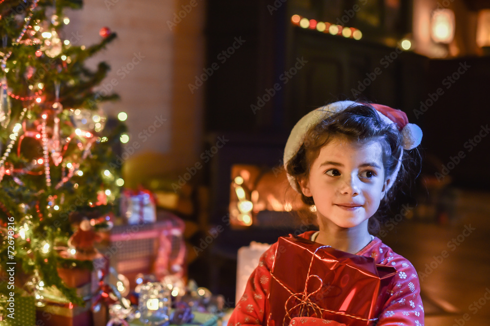 Lovely little girl opens a gift in front of the Christmas tree l