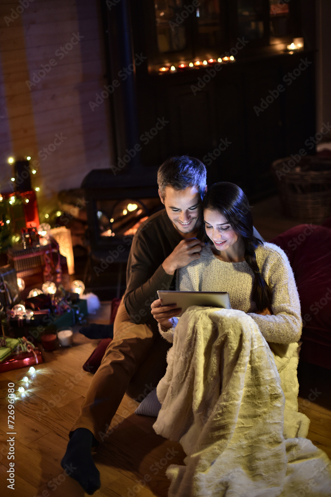 Romantic couple sharing a digital tablet near a wood stove, enjo