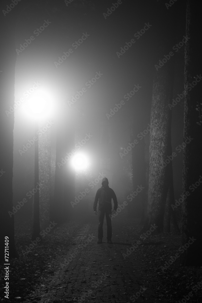 Scary man standing in a lane on a foggy night. Black and white.