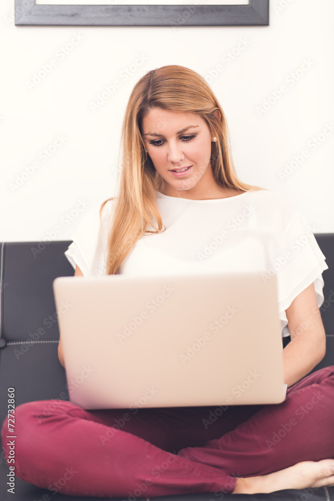 Smiling young woman looking on your laptop sitting on sofa at ho Smiling young woman looking on your laptop sitting on sofa at ho