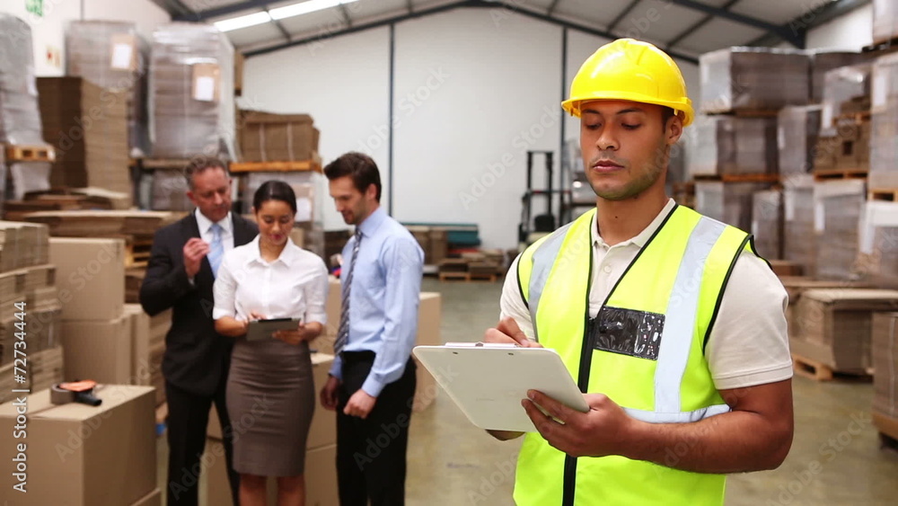 Warehouse managers talking while worker uses tablet pc Warehouse managers talking while worker uses tablet pc