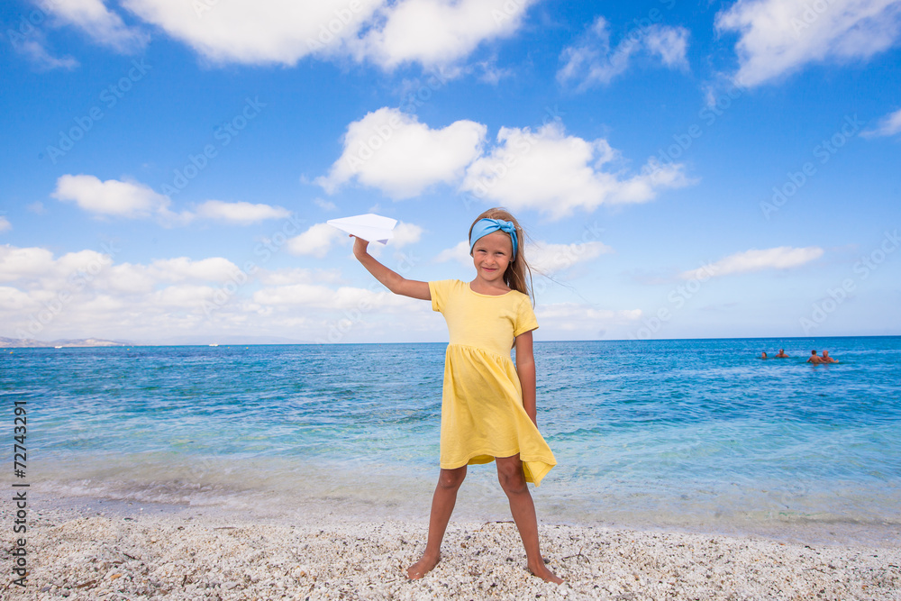Happy little girl with paper airplane during beach vacation
