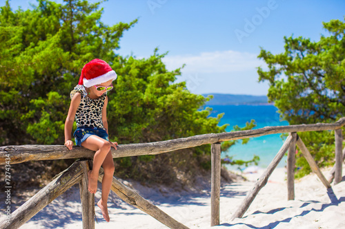 Fototapeta Naklejka Na Ścianę i Meble -  Adorable little girl in christmas hat during summer beach