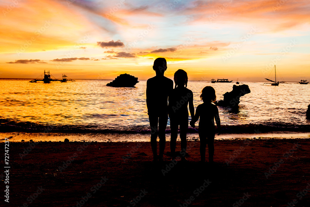 three kid silhouettes on sunset sea background