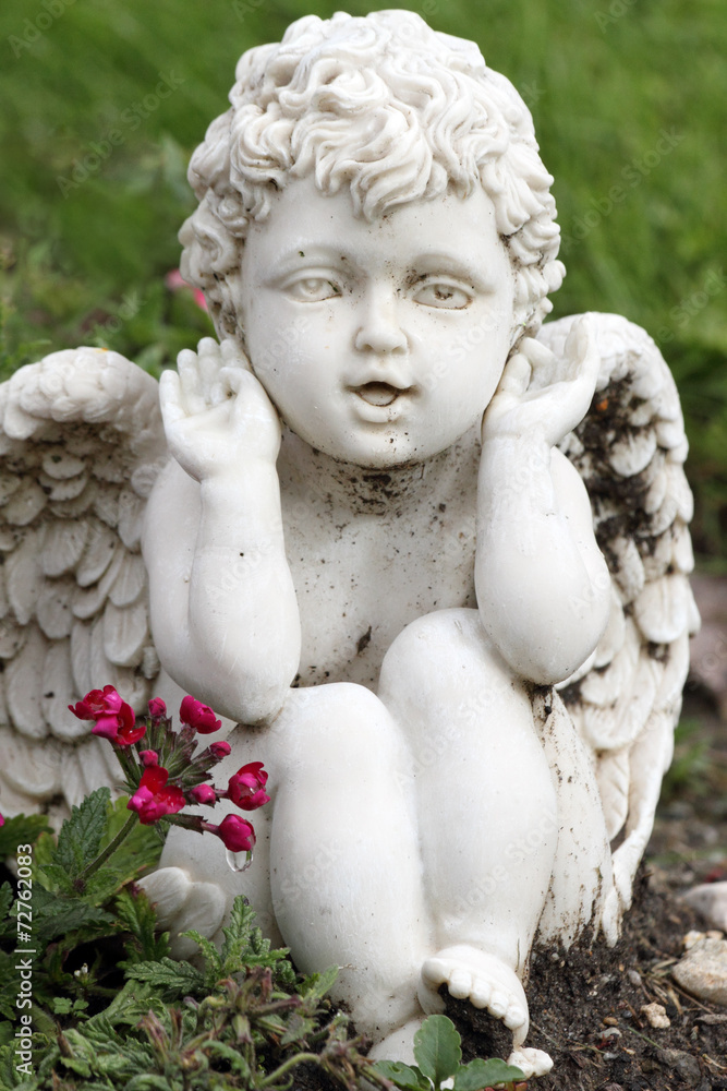 playful angelic figurine sitting in garden on flowerbed
