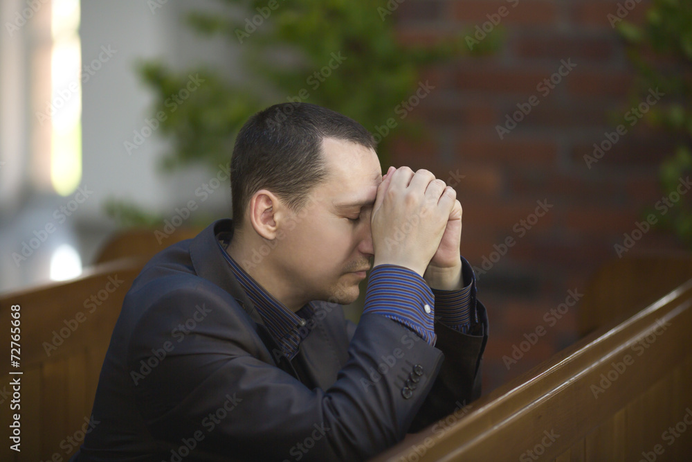 Handsome young man praying in a church Handsome young man praying in a church