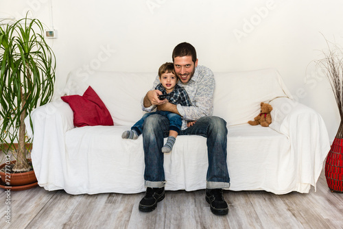 Baby and father watching tv and smiling on a white sofa © giacomoprat