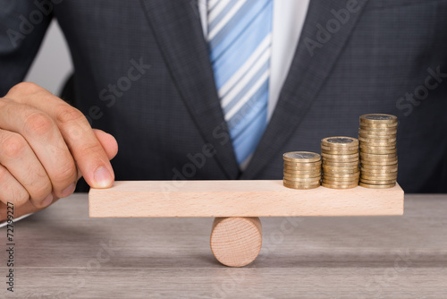 Businessman Balancing Coins On Wooden Seesaw photo