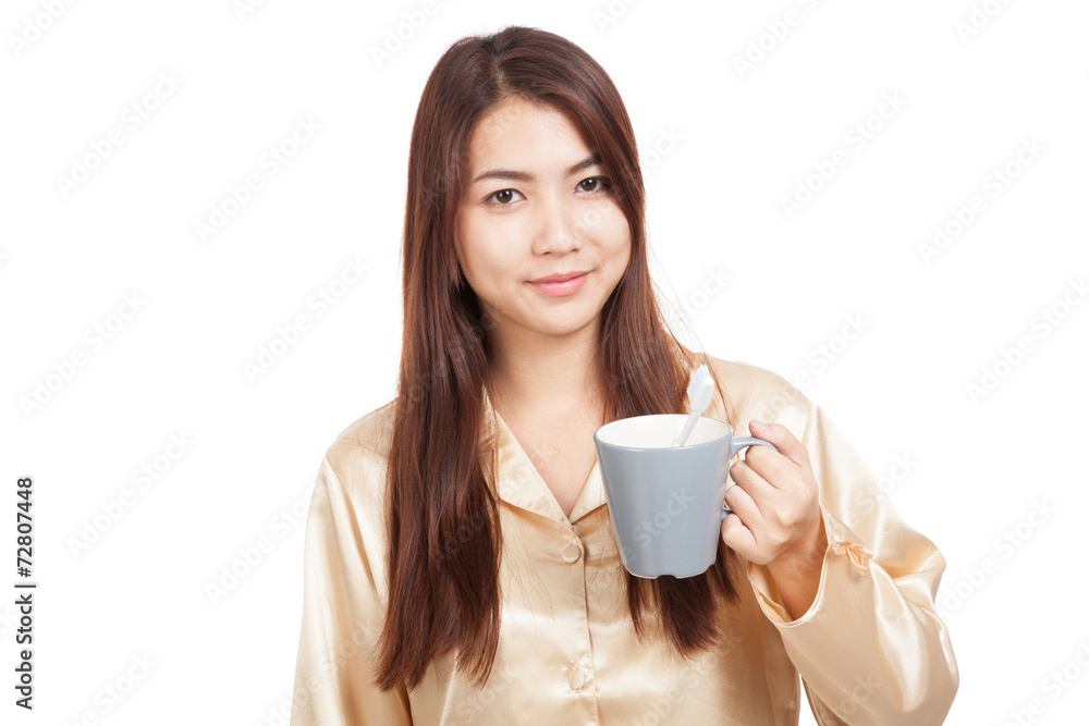 Asian woman in pajamas with toothbrush in mug Asian woman in pajamas with toothbrush in mug