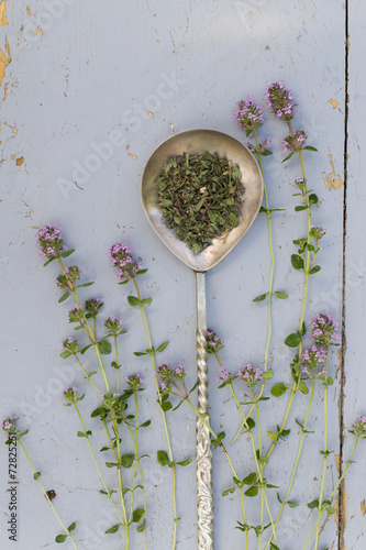 Thyme sprigs with dried in a spoon on a rustic wood table.