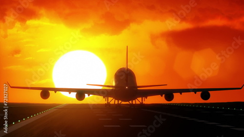 Plane lands on airport runway in front of large sunset