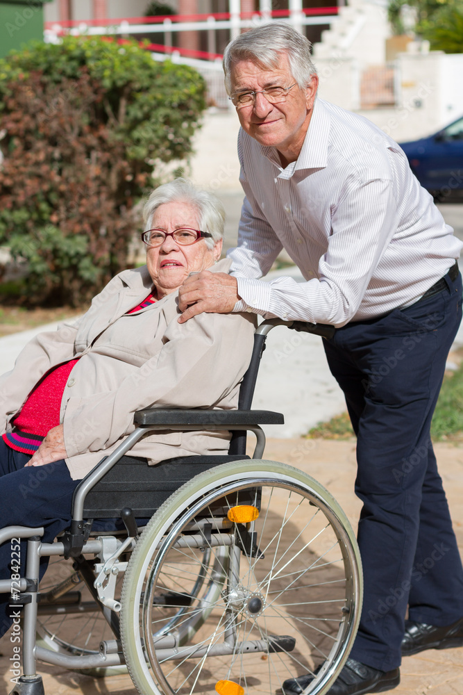 Man walking with senior woman in a wheelchair in park Man walking with senior woman in a wheelchair in park