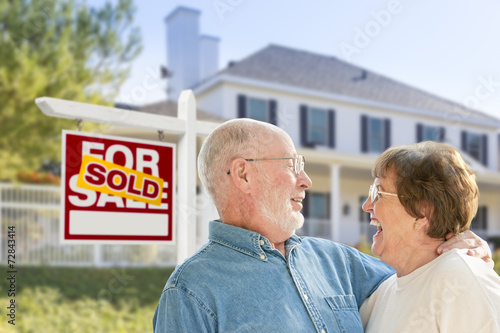 Senior Couple in Front of Sold Real Estate Sign, House