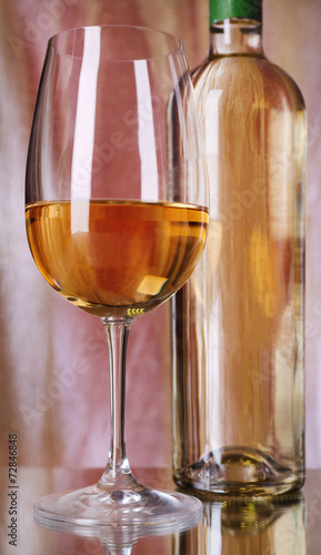 Wine bottle and wineglass with white wine on bright background