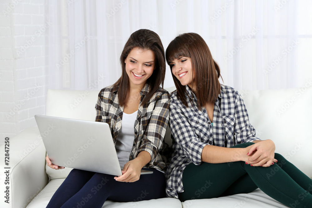Fototapeta premium Beautiful girls twins sitting on sofa with notebook in room