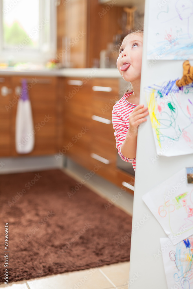 Cute little girl sticking tongue out behind refrigerator door in Cute little girl sticking tongue out behind refrigerator door in